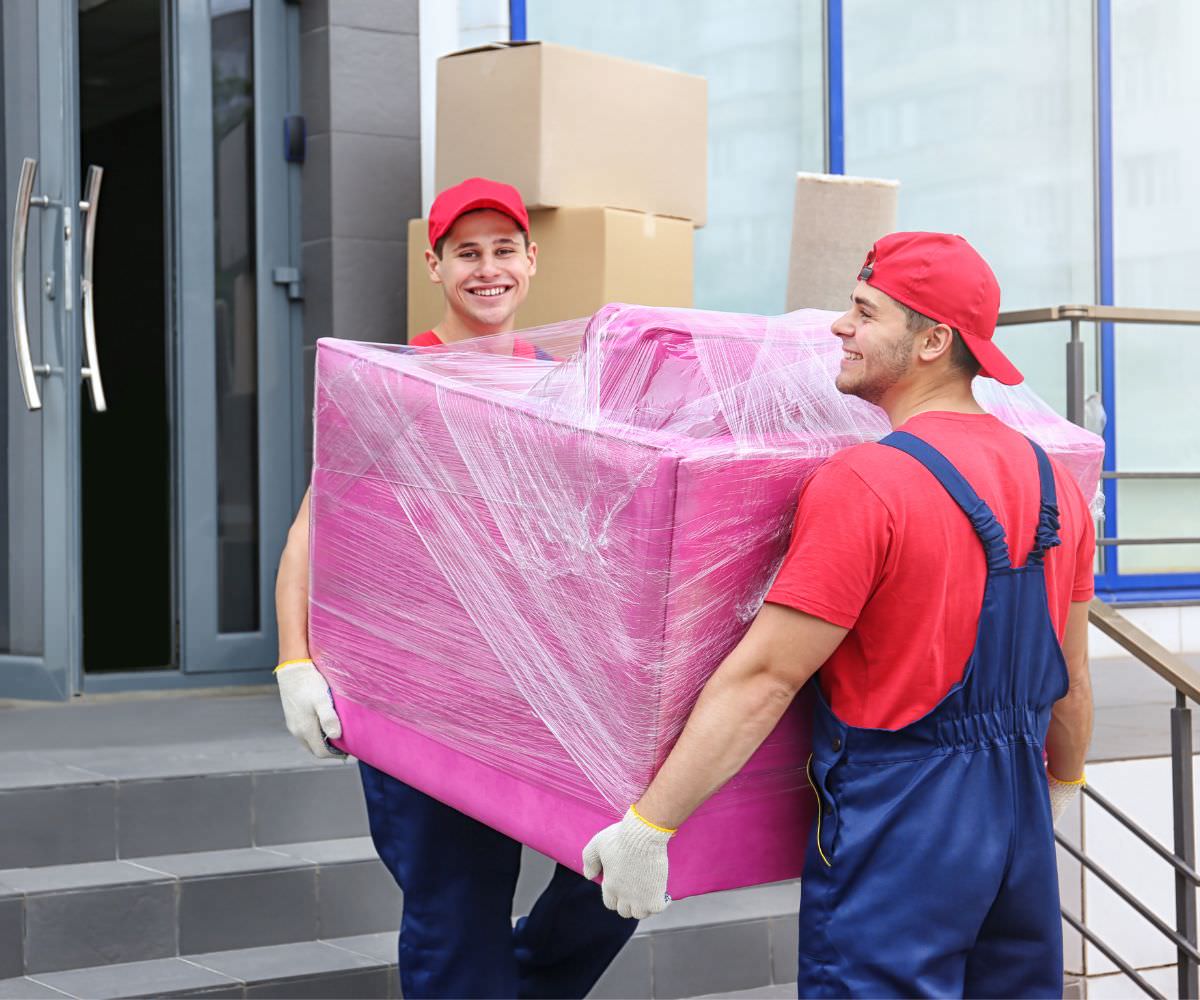 Zwei Umzugshelfer tragen ein in Folie gepacktes Möbelstück